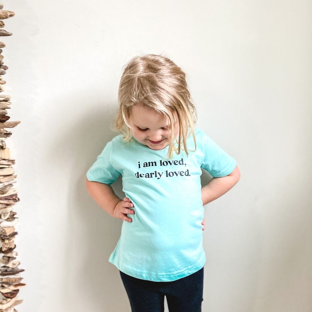 little girl looking down at the shirt wearing the loved shirt and black leggings.