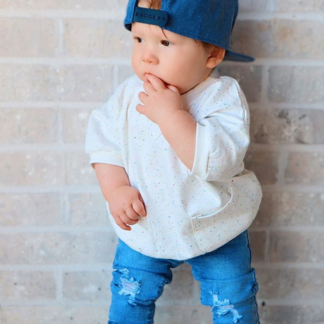 baby in the sweatshirt tee in sprinkles, blue jeans, and a matching cap.