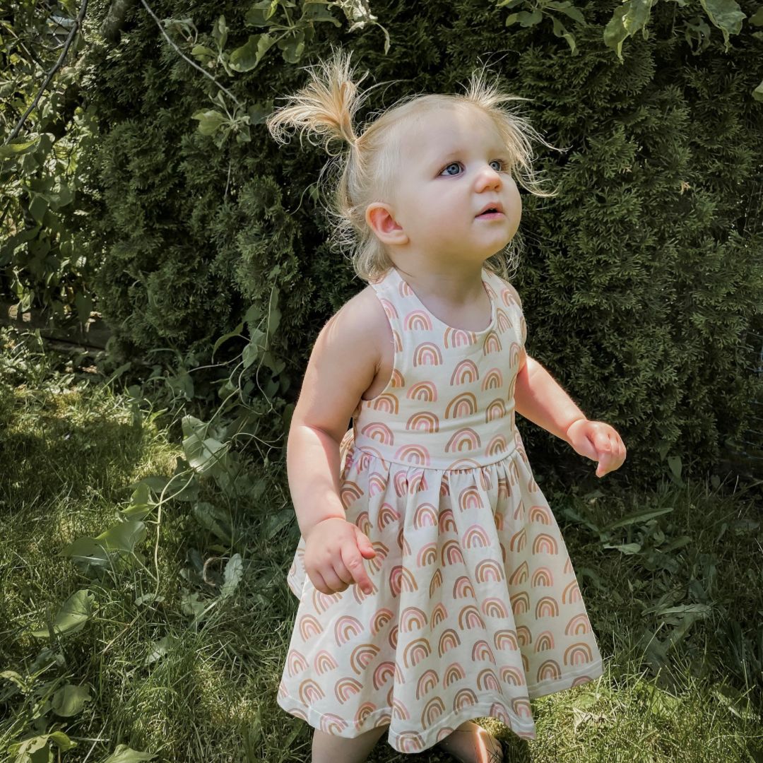 Baby girl looking off camera wearing the Sofia dress in muted rainbow.