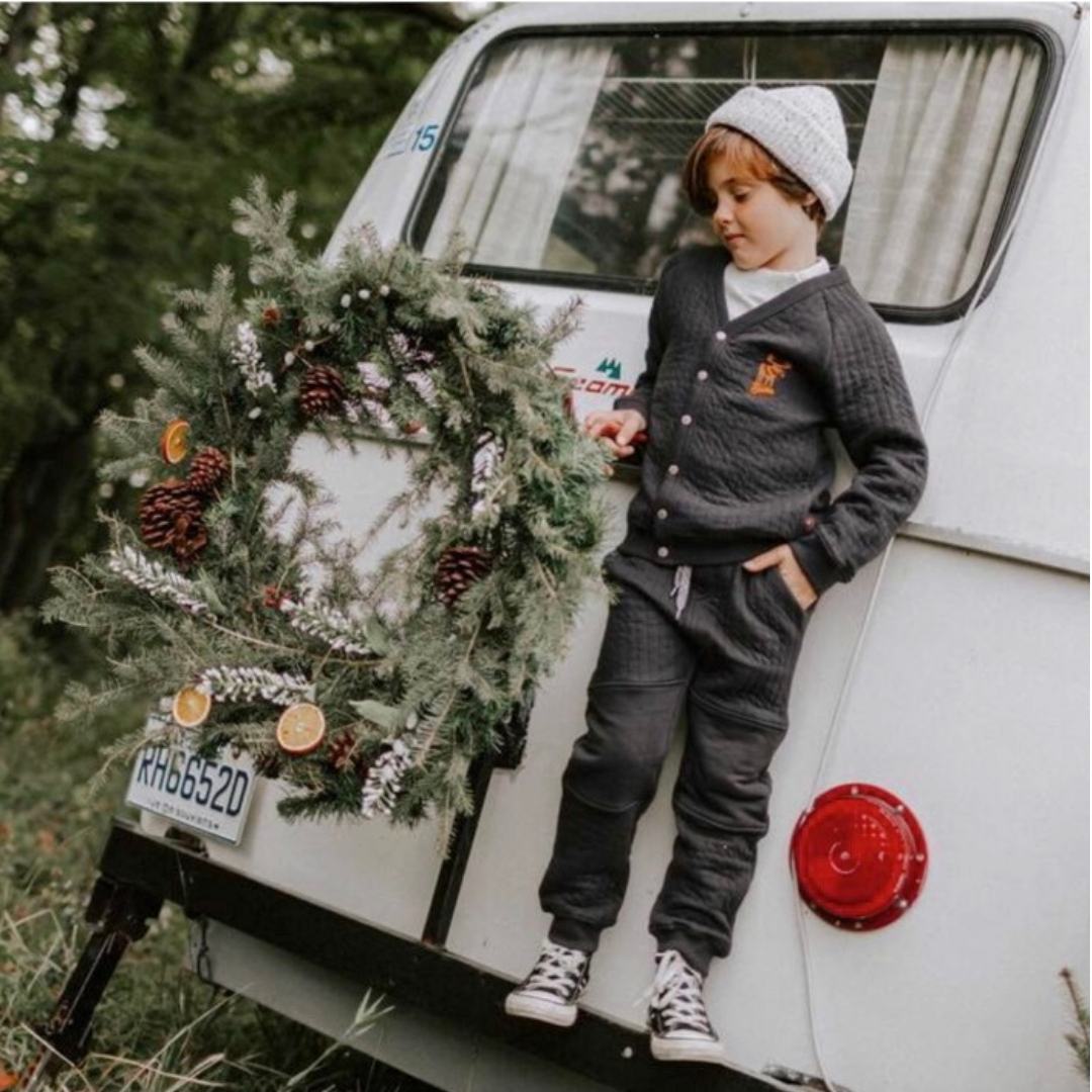 Boy standing on the back of a van with a winter wreath wearing the quilted joggers in charcoal and converse sneakers