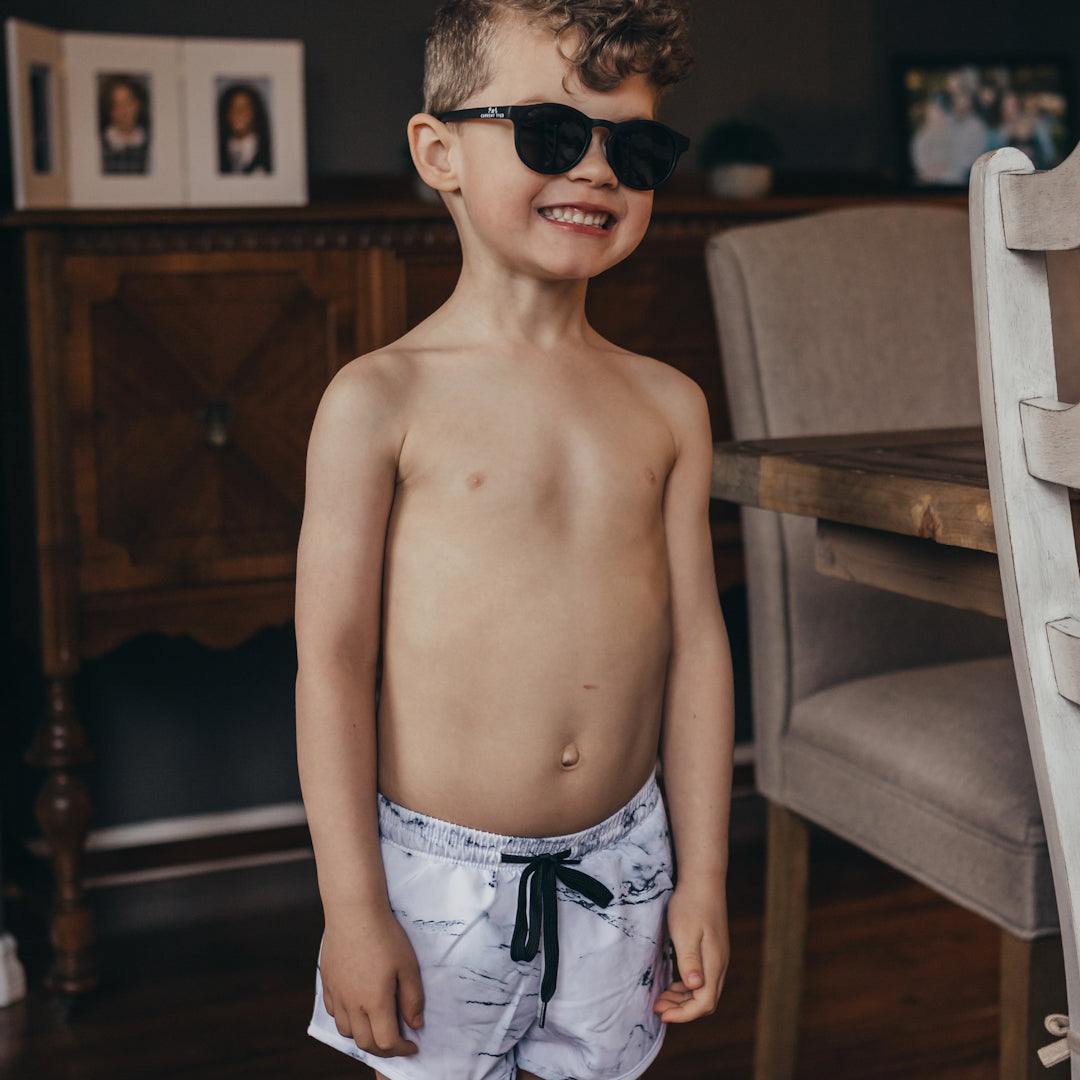 Smiling little boy wearing a the tye boardies which are a marble print euro style board short