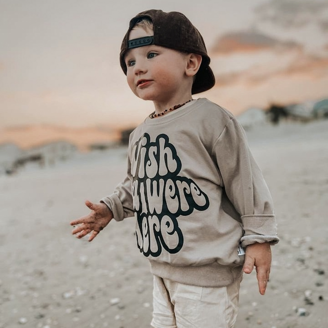 Toddler boy in a neutral beige pullover sweatshirt with wish you were here printed on the front.