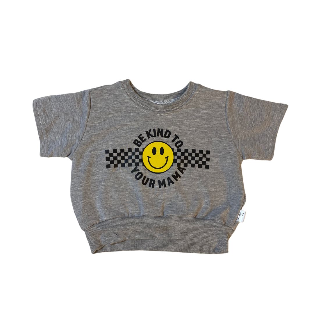 Short sleeved retro fit baby and toddler sweatshirt in heather grey. The front says "be kind to your mama" in black around a yellow smiley face and a checkerboard racing stripe.