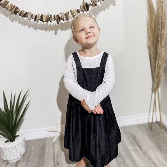 three year old girl wearing the apron dress in black denim.