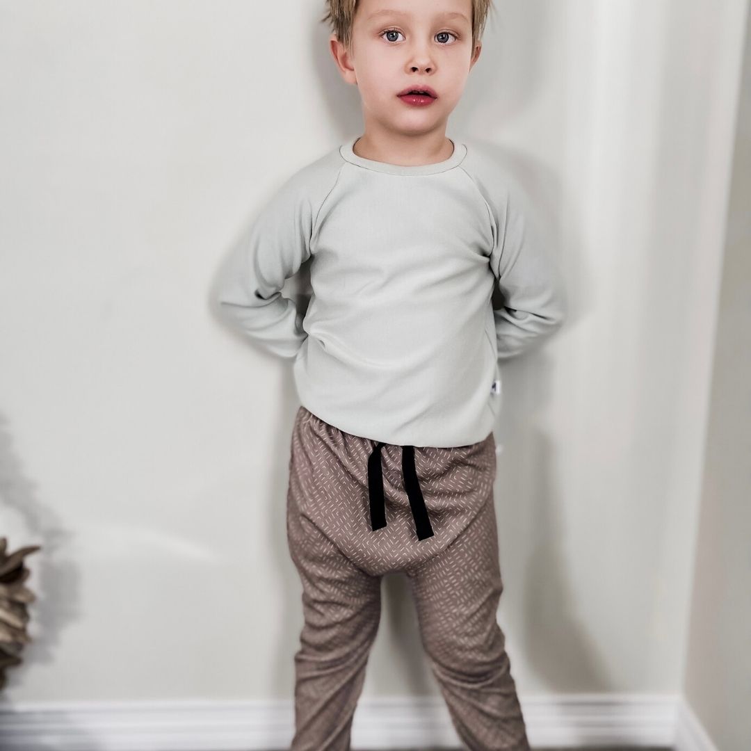 Boy wearing the harem pants in neutral grid print with a black faux drawstring paired with the raglan pullover sweater in mint.