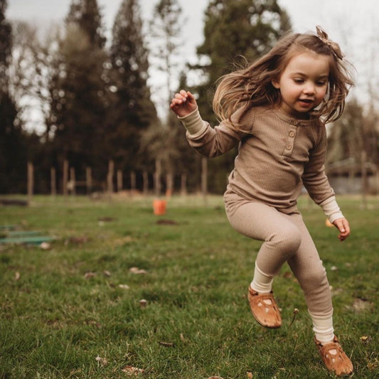 Toddler girl jumping in a neutral outfit featuring the waffle set in taupe