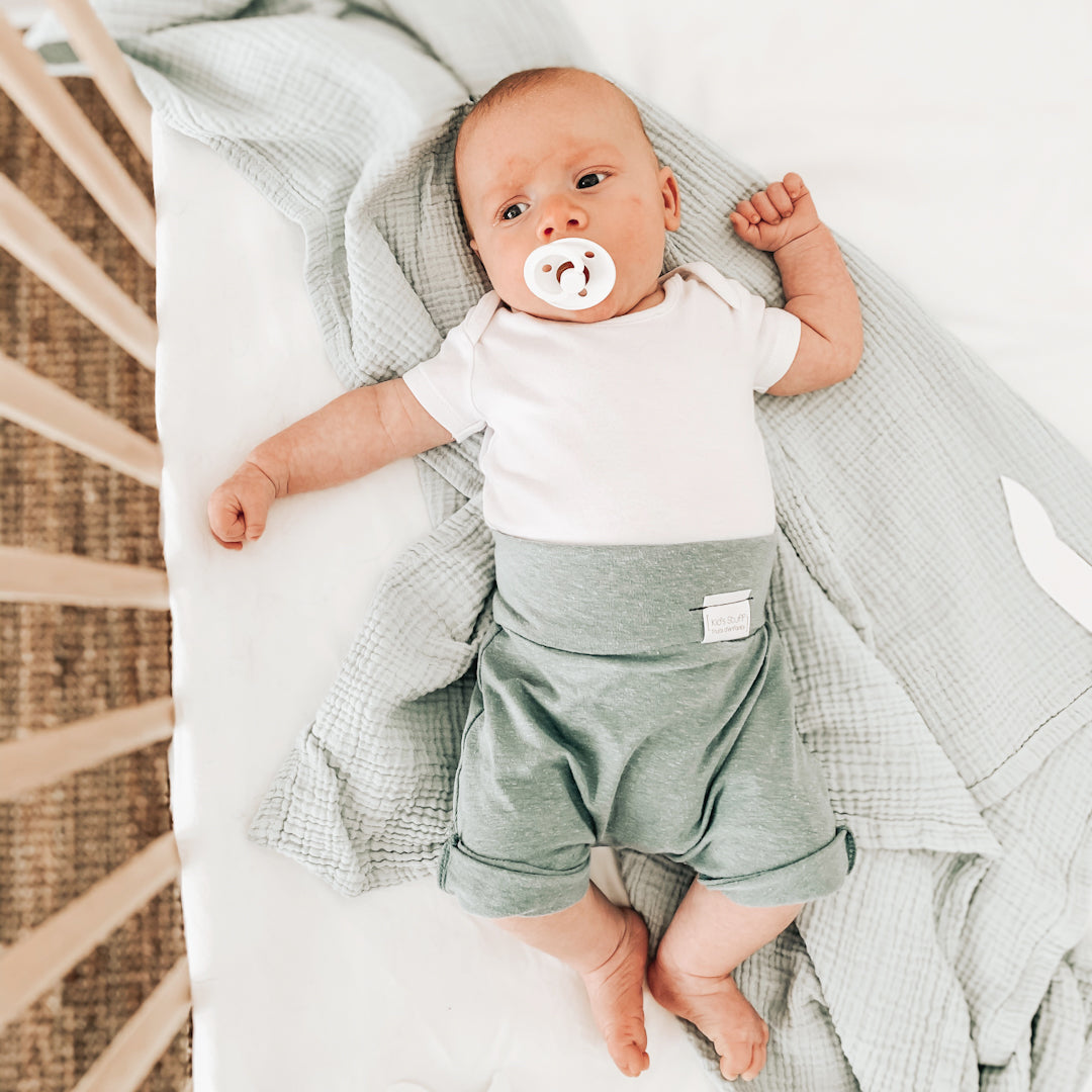 Baby boy in a crib wearing the grow with me shorts in mineral blue