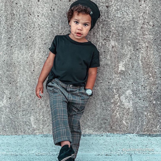 Stylish toddler boy wearing the garbardine pants , and matching black shirt, loafers, and beanie.