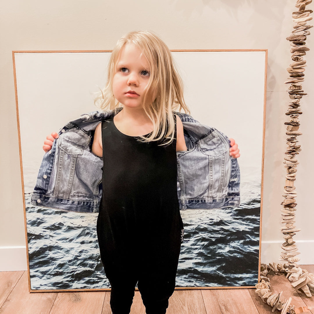 Three year old blonde girl wearing the romper in black with a denim jacket.