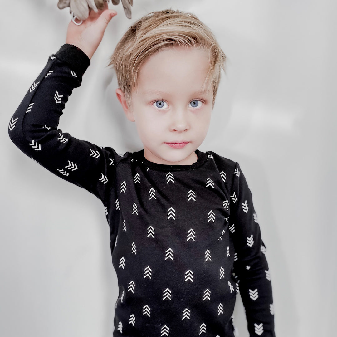 Blond boy facing the camera wearing a black long sleeved shirt with triple arrow pattern in white printed all over the shirt.