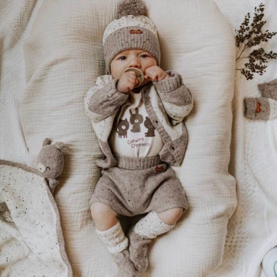 Picture of a baby in the 2 way cardigan in stone and the matching shorts laying on a pillow.