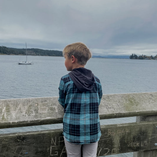 Boy in the hooded flannel in ocean staring at the ocean