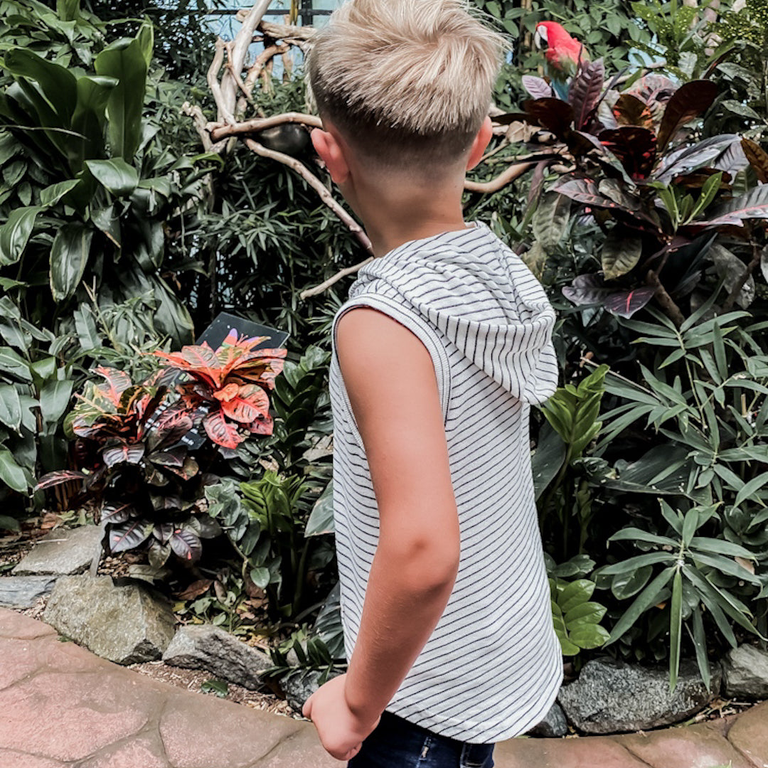Lifestyle Photo of a boy in a tropical garden wearing the Black and White striped sleeveless hoodie by Orcas Lucille 