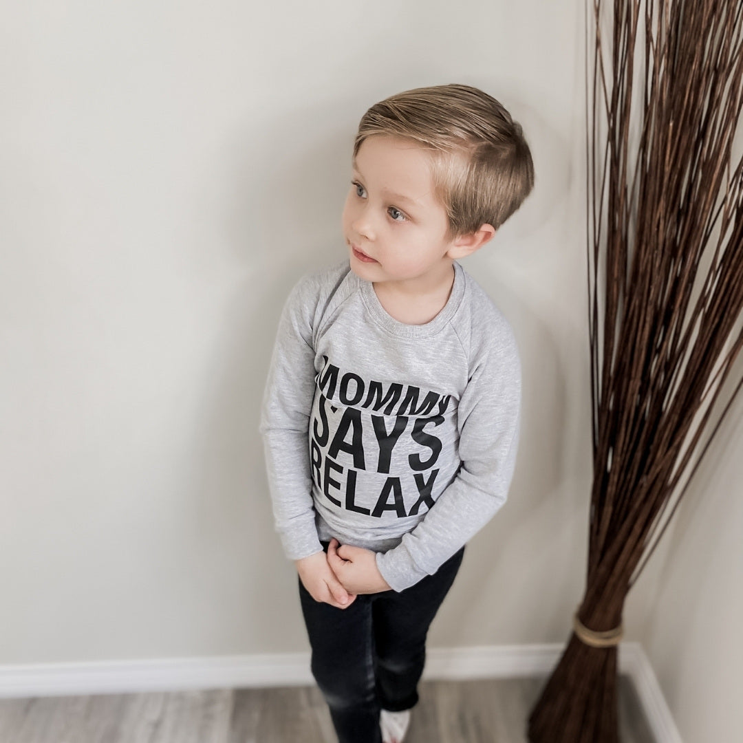 Four year old boy wearing the mommy says relax raglan pullover sweater in light grey with black jeans and white converse.