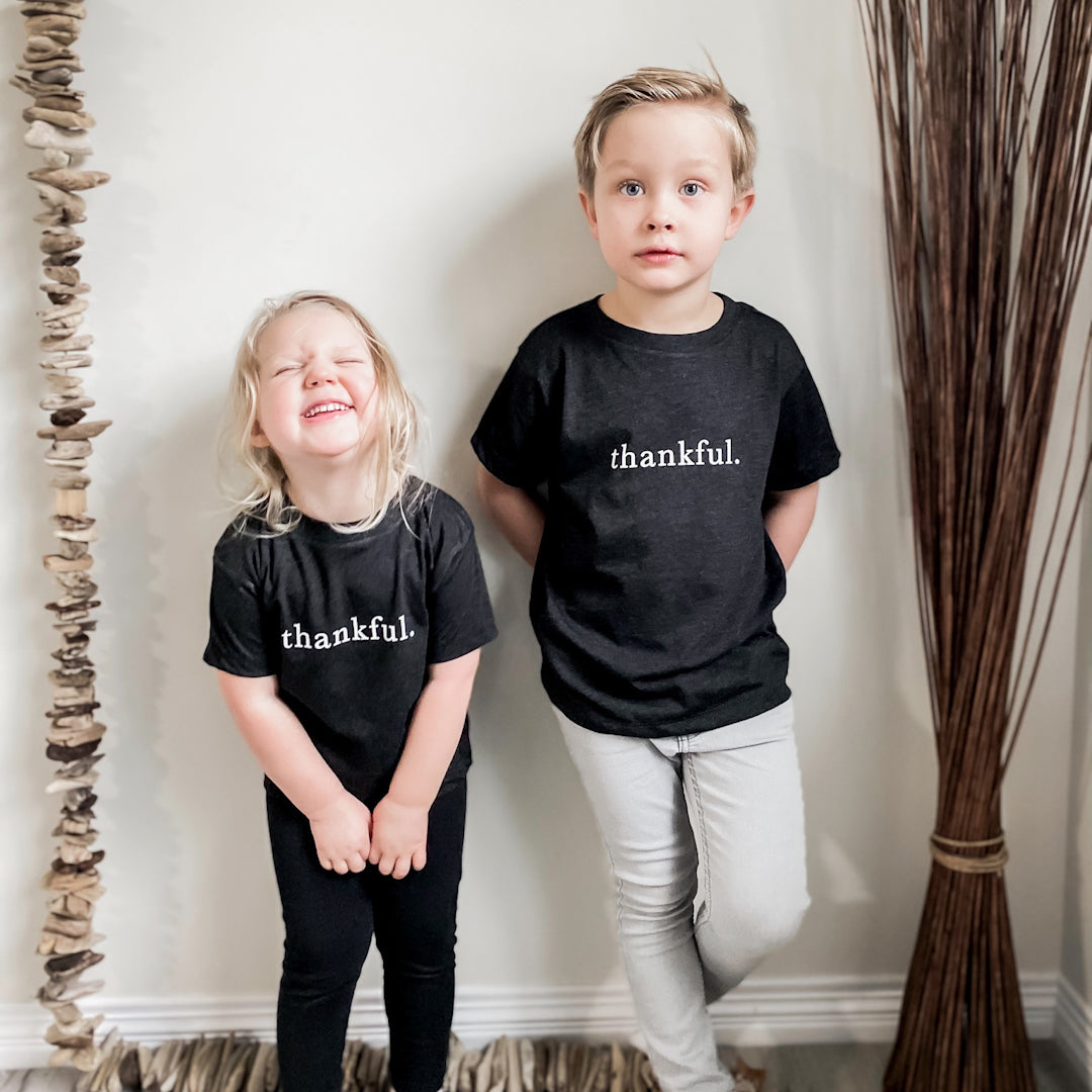 Blonde boy and girl looking at the camera. Girl is laughing. Both are wearing the thankful shirt in heather charcoal grey.