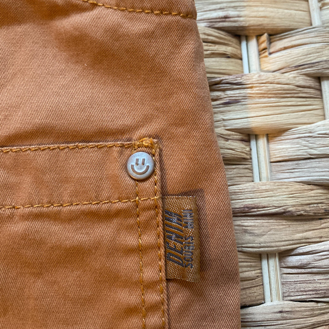 Close up detail shot of the denim overalls in terracotta''s happy face grommets.