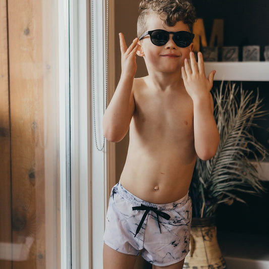 curly haired boy wearing sunglasses near a glass door wearing the tye boards with a marble print.