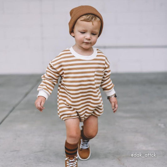 Adorable toddler boy in a neutral outfit, including the sweatshirt romper in neutral stripes and matching beanie, socks, and boots.