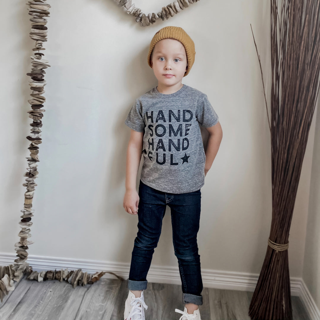 Little boy wearing the handsome handful shirt in heather grey with blue jeans and a yellow toque.
