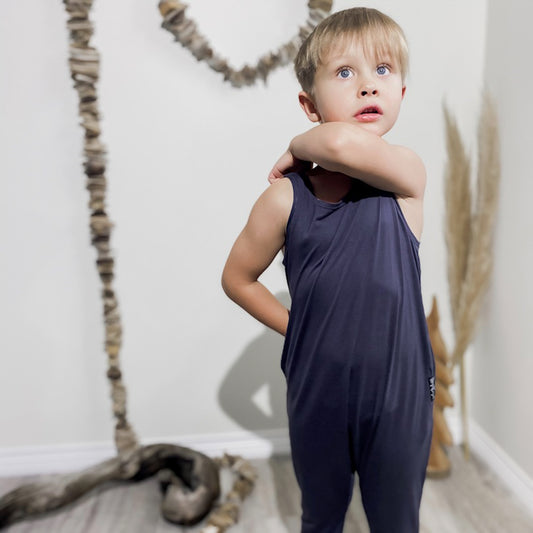 Four year old blonde boy scratching his shoulder wearing the romper in slate blue