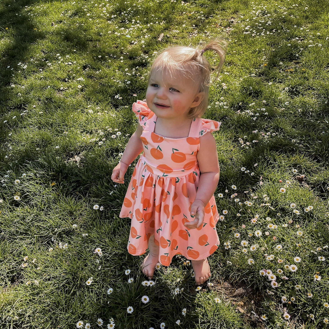 Baby girl wearing the Rosita dress in peachy.