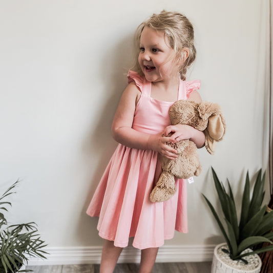 blonde three year old wearing the Rosita dress in pink peony holding a tan coloured bunny.