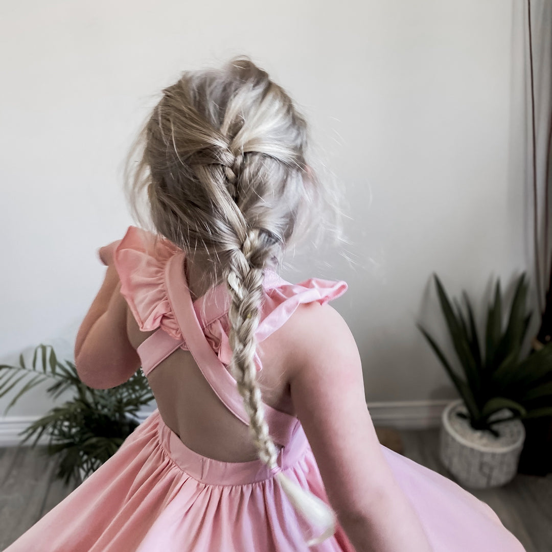 Blonde girl showing off the criss crossed ruffle straps and full circle twirl skirt of the Rosita dress in pink peony.