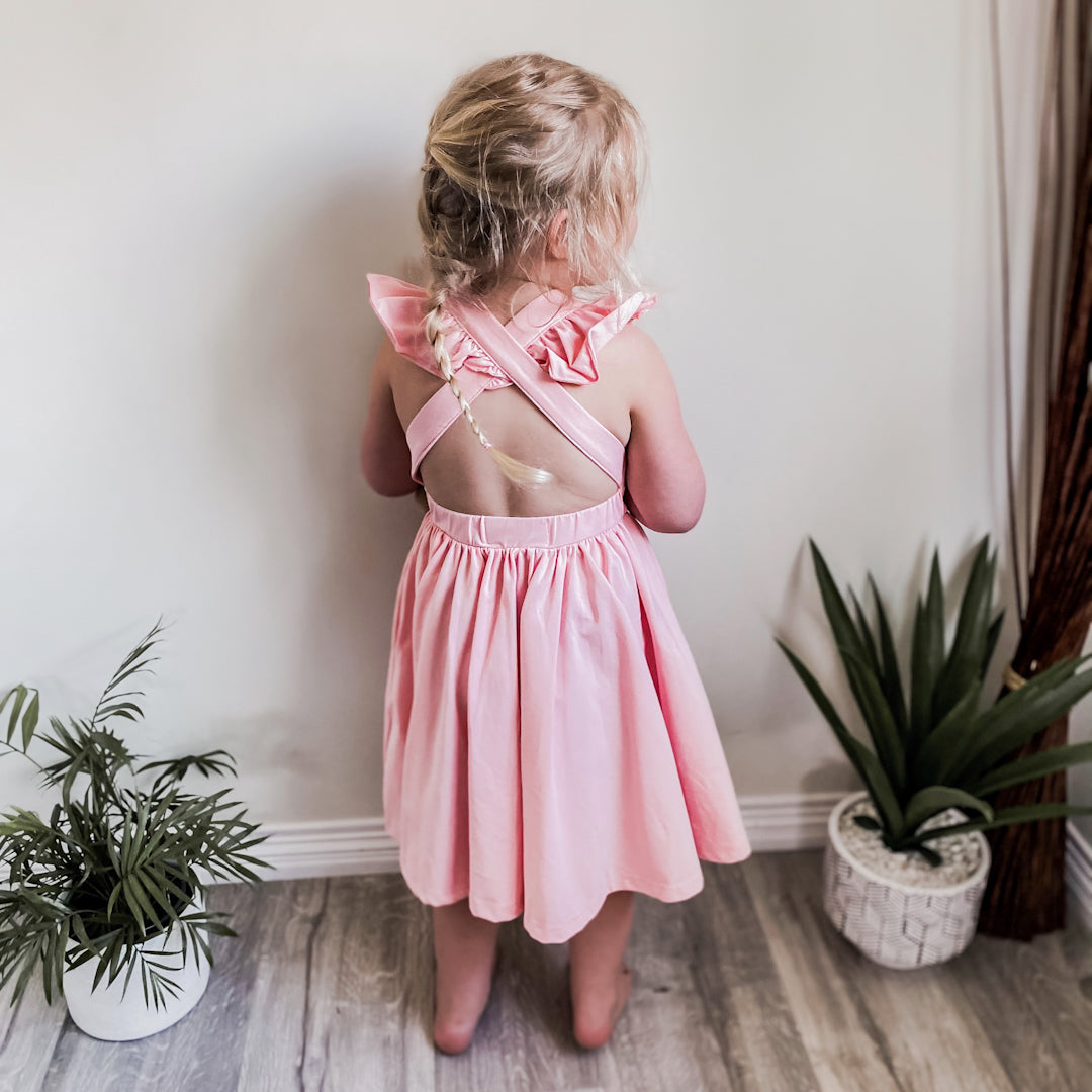 Little girl showing off the criss crossed ruffle straps and open back of the Rosita dress in pink peony